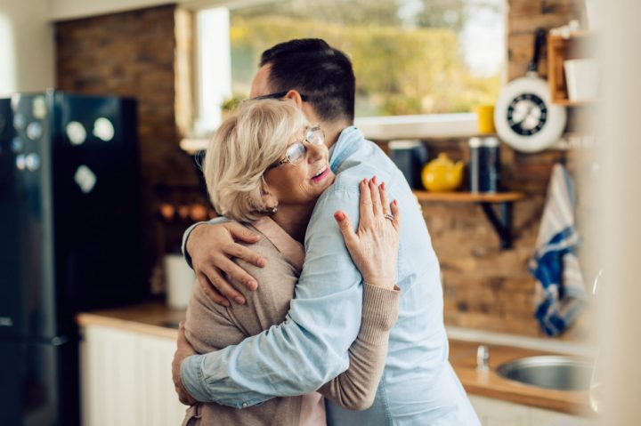 Happy mature woman and her adult son embracing in the kitchen.